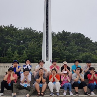 주간보호센터 이용자들이 기념비 앞에 앉아 꽃받침 포즈를 하고 찍은 단체사진